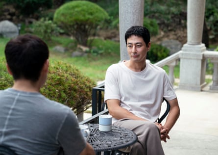 Zo In-sung as Sang-woo sits at an outdoor table, talking to another person.