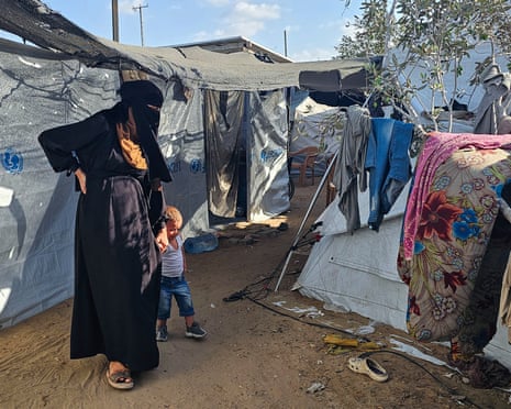 A pregnant woman wearing a burqa walks with a small boy between makeshift camps in Gaza