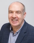 Fin McCaul: he is a middle-aged man with balding grey hair and is wearing a grey-blue tweedy jacket with black checks and a button-down shirt