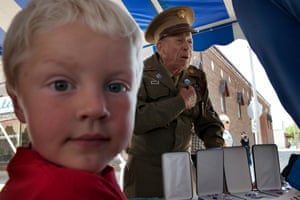 A child in the foreground looks into the camera as the veteran behind points to the medals on his chest