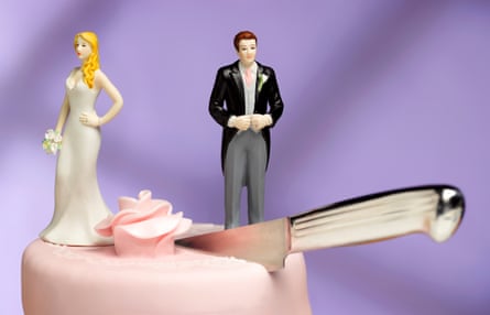 Top of pink wedding cake with figurines of the bride and groom, facing away from each other and looking despondent, with cake cut by a knife halfway between them