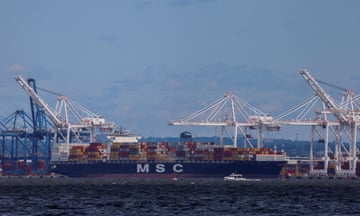 A small boat on the water can be seen next to a cargo ship near a boat terminal