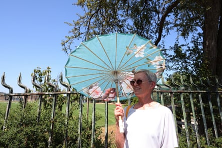 Julith Jedamus holding a parasol while standing next to a fence bordering the green pitch