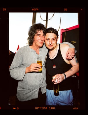 Howard Marks and Shaun Ryder, holding drinks, smile at the camera in front of a dawn sky