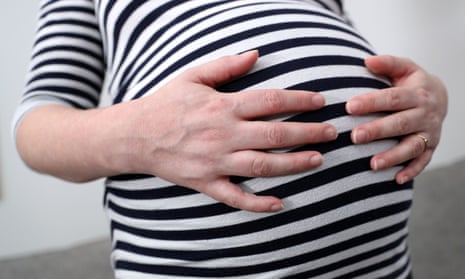 A pregnant woman holds her stomach wearing a striped top