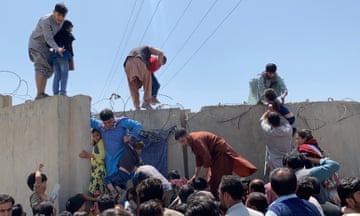 People standing on top of a wall helping others from the crowd below try to climb it.