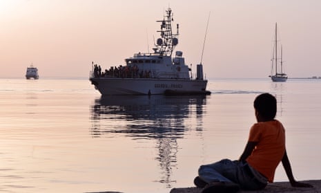 A boy watches an Italian Frontex vessel loaded by intercepted  migrants arriving to the port of Kos.