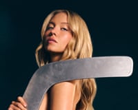 Sydney Sweeney rests a large metal hockey stick blade on her bare shoulder