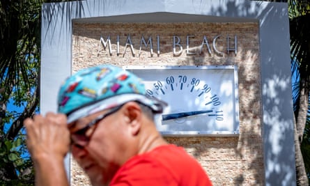 A person walks in front of a Miami Beach clock thermometer that marks the temperature at 105F (about 40C) during the hottest summer in modern history on 30 July 2023.