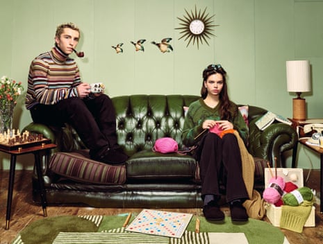 Young couple sitting on a sofa as if they're old people, him smoking a pipe, her knitting, rollers in her hair, flying ducks behind them on the wall