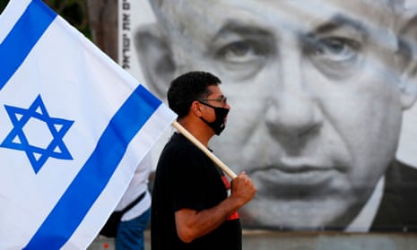 A protester carries the Israeli flag in front of a poster of Benjamin Netanyahu