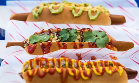 Três cachorros-quentes com coberturas incluindo ketchup e mostarda e folhas de coentro
