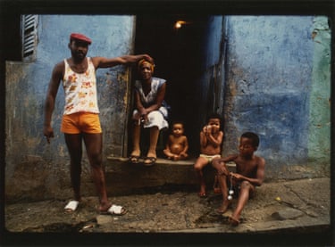 a man standing beside woman and three children seated outside building