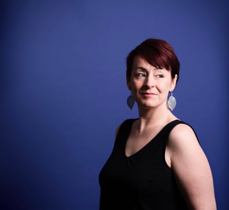 Leesa Morris photographed from the waist up at angle to the camera and looking to her left, wearing a black sleeveless top and large, leaf-shaped earrings, against a dark-blue background