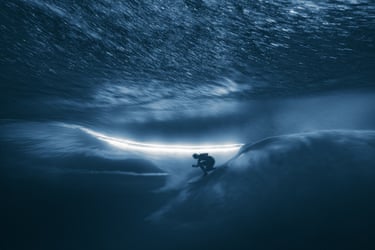 Underwater view of a surfer silhouetted on a Teahupo’o wave beneath swirling light