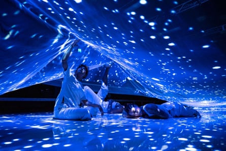 Performers under a sheet illuminated to look like the night sky
