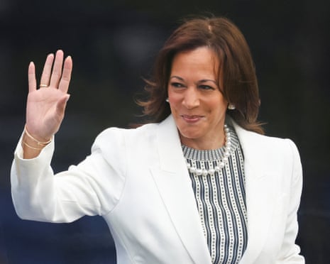 woman in a white blazer smiles and waves
