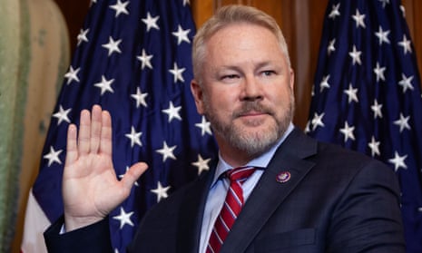 A man wearing a suit holds up his hand, American flags behind him