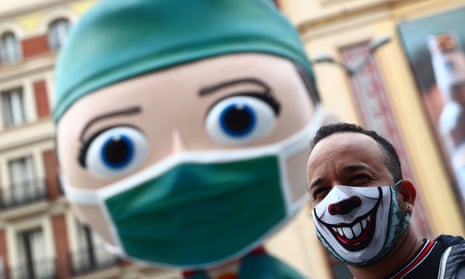 A man wearing a protective face mask poses for pictures next to an oversized model of a health worker in Madrid.