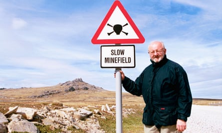 Gareth Parry standing by a minefield sign with Mount Tumbledown in background in East Falkland, 2015.