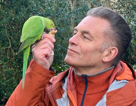 Chris Packham looking at a parakeet who is eating a nut from his hand