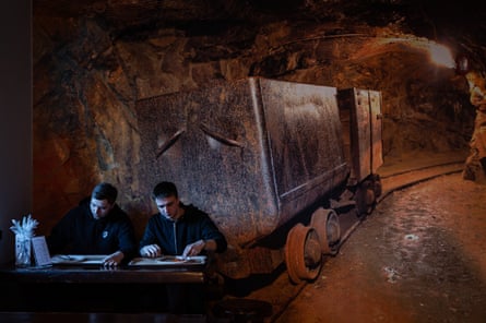 Two students are having lunch in front of a large poster depicting a mining tunnel with a mine car