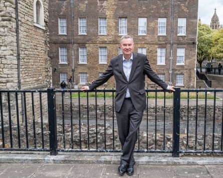 David Gauke standing against black iron railings in front of stone buildings. He wears a dark grey suit