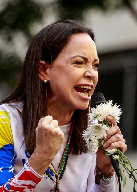 Machado with fist clenched and flowers in the other hand speaks into a microphone