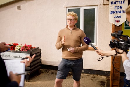 In a light-brown top and shorts, wearing spectacles and with ginger-blonde hair, local parish councillor Joe Marshall is interviewed on camera