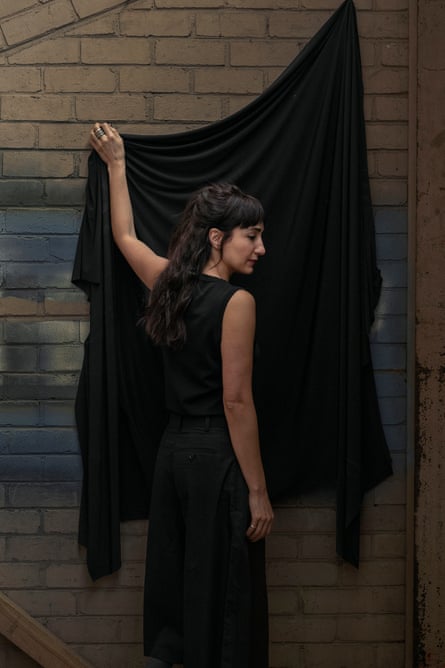 Artist Hoda Afshar stands against a brick wall, pulling down a large black cloth