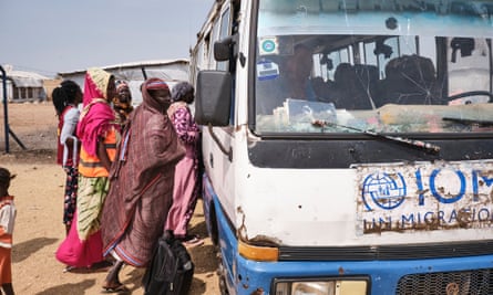 A group of women stand next to a small and battered blue and white bus