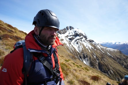A mountaineer wearing a helmet in front of a snow-covered peak