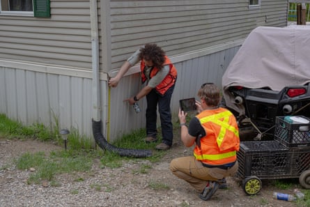 a man points at base of home outside as another man crouches down and takes a picture