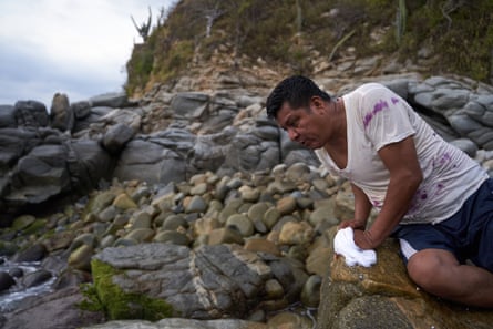 A man leans over a rock for a closer look on a rocky beach