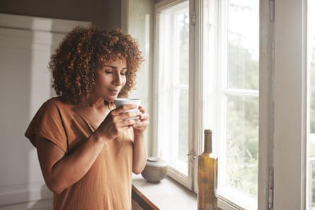 Woman smelling coffee by windowMature woman smelling coffee standing by window in bedroom