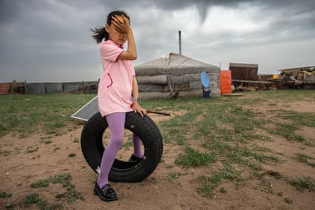 A girl sitting on a tyre shields her eyes from dust