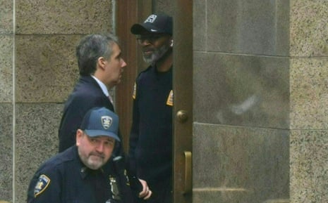 a man with grey hair walks past two police officers into a stone building