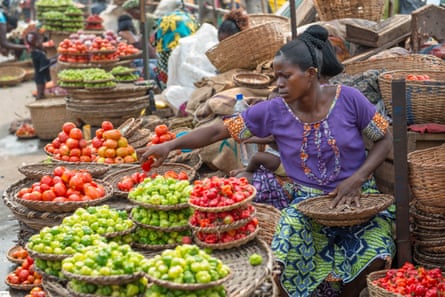 A woman in a purple blouse and green skirt selling chilies from baskets stacked one on top of the other