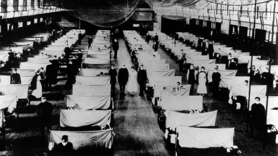 Rows and rows of beds with material screens between them in a field hospital set up in a warehouse during the 1918 pandemic.