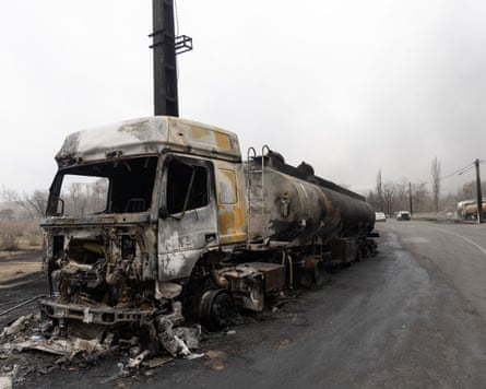 A burnt truck with no windows and debris around it on a road