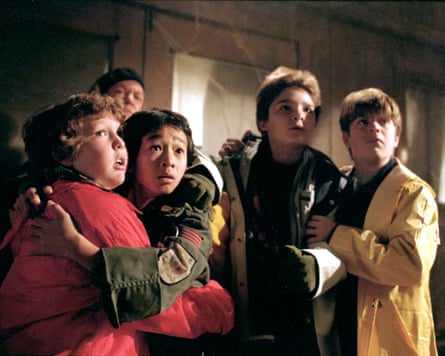 A group of children nervously hug each other with an adult just visible behind