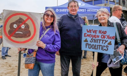 Three people holding protest banners on the beach