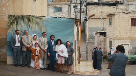 A person takes a photo of a family posing on a tropical backdrop in the middle of a city street
