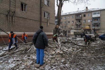 Rubble on road with people in hi-vis clearing and residential buildings in background