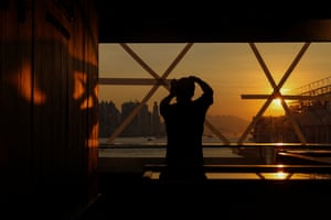A shop worker tapes a glass window in preparation for a storm, the sun sets in the distance