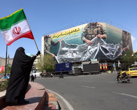 A woman holds Iran's national flag while standing near a billboard with a sentence reading 'The Strait of Hormuz remains closed' at the Enqelab Square in Tehran, on 5 April 2026.