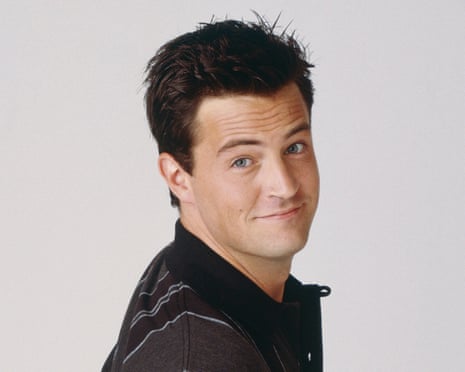 He smiles at the camera, mouth closed, eyebrow cocked slightly