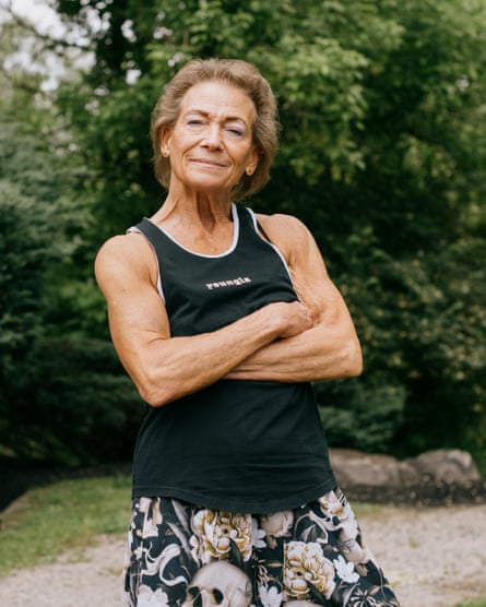 Marlene Flowers standing in black vest top with folded arms outside with bushes and trees behind her.