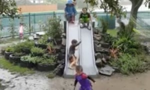 A still from the video showing children gleefully leaping down the slide into a muddy puddle in the middle of a rainstorm.