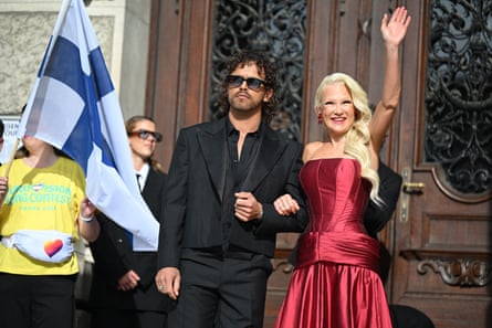 Linda Lampenius and Pete Parkkonen outside wooden door with Finnish flag to their right